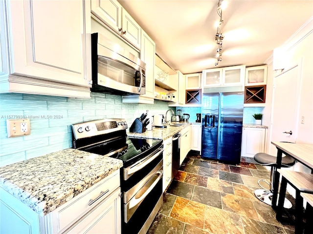 kitchen with appliances with stainless steel finishes, dark tile floors, backsplash, track lighting, and light stone countertops