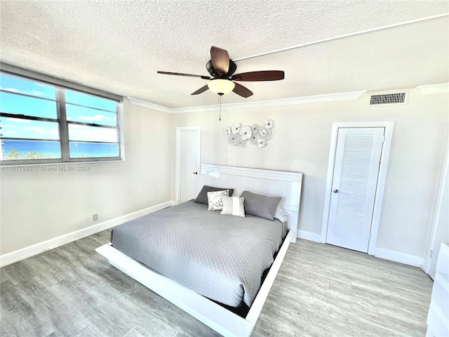 bedroom with ornamental molding, wood-type flooring, ceiling fan, and a textured ceiling