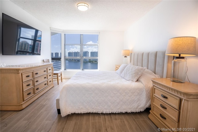 bedroom featuring wood-type flooring, a textured ceiling, a water view, and expansive windows