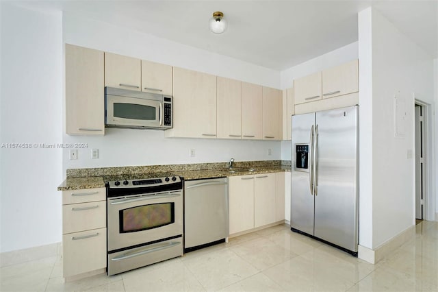 kitchen with appliances with stainless steel finishes, sink, light tile floors, and dark stone countertops