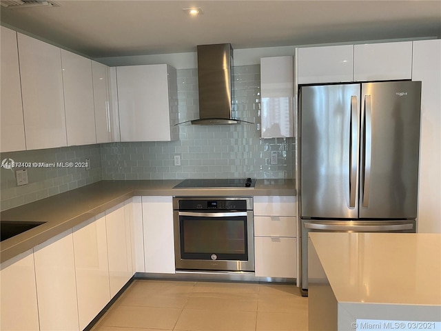 kitchen featuring appliances with stainless steel finishes, backsplash, wall chimney range hood, and white cabinetry