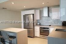 kitchen with wall chimney exhaust hood, a kitchen island, tasteful backsplash, white cabinetry, and stainless steel appliances