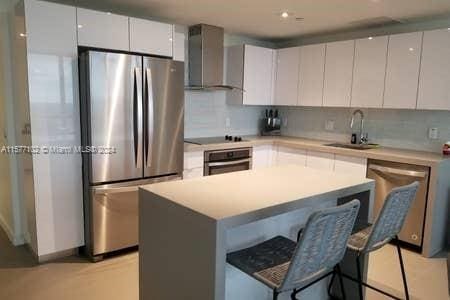 kitchen featuring appliances with stainless steel finishes, a kitchen island, wall chimney exhaust hood, and white cabinetry