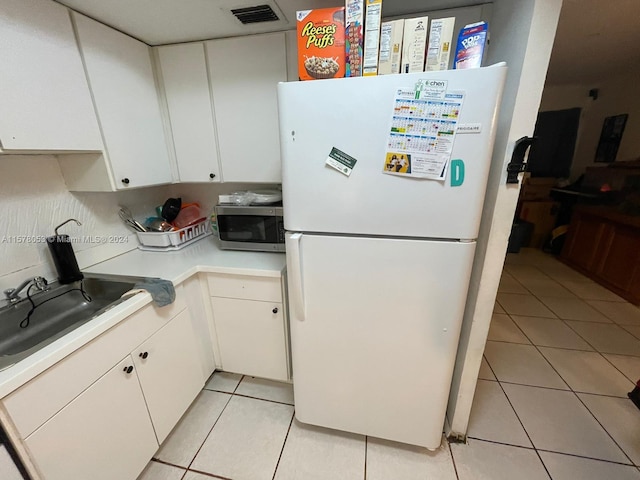 kitchen with white cabinets, white fridge, sink, light tile floors, and tasteful backsplash