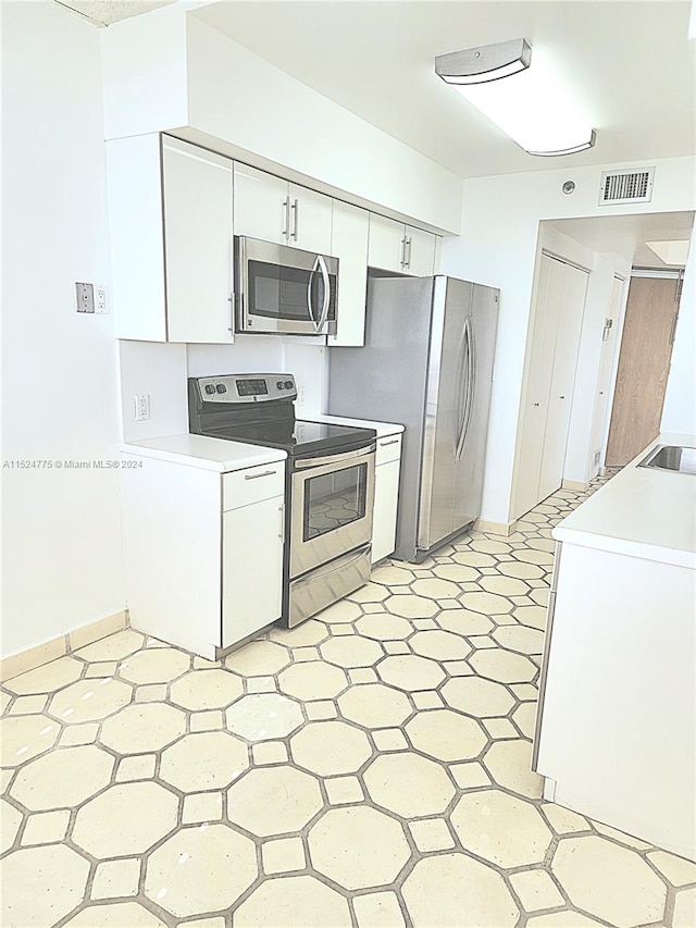 kitchen with stainless steel appliances, white cabinetry, and light tile floors