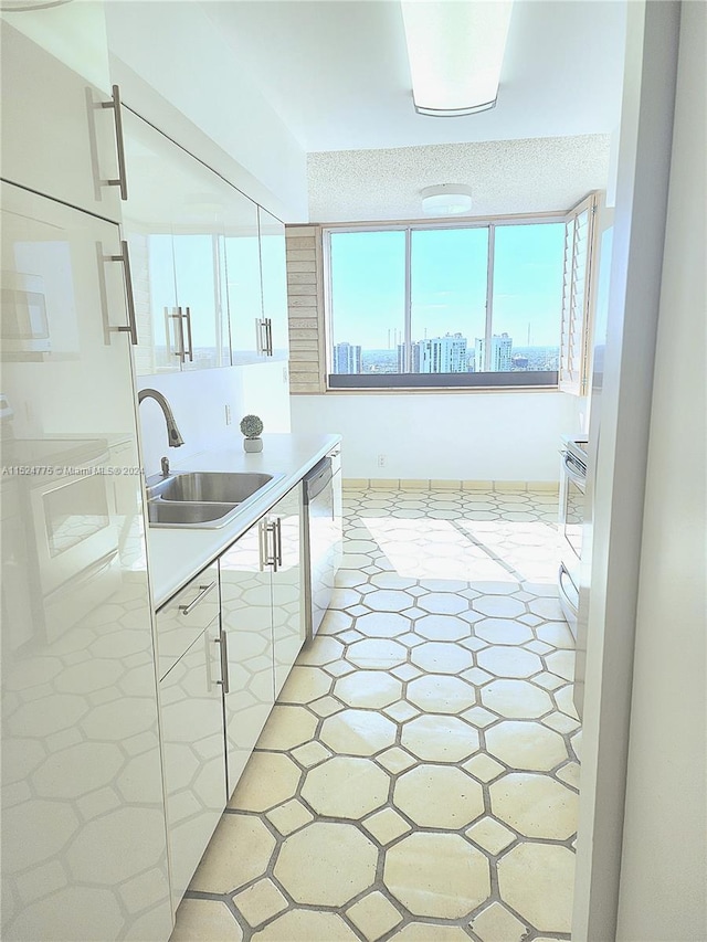 kitchen featuring a textured ceiling, white cabinets, sink, light tile floors, and stainless steel dishwasher