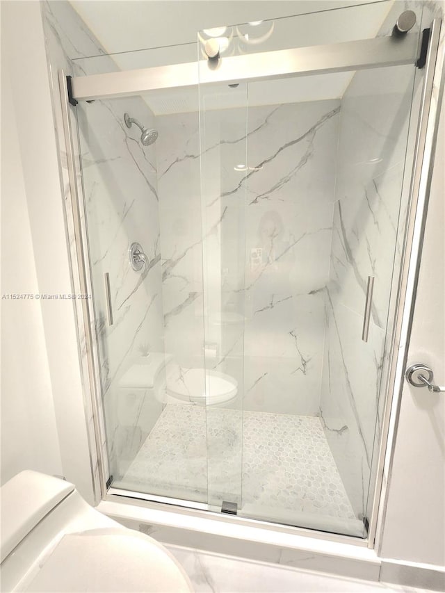 bathroom featuring a shower with door and toilet