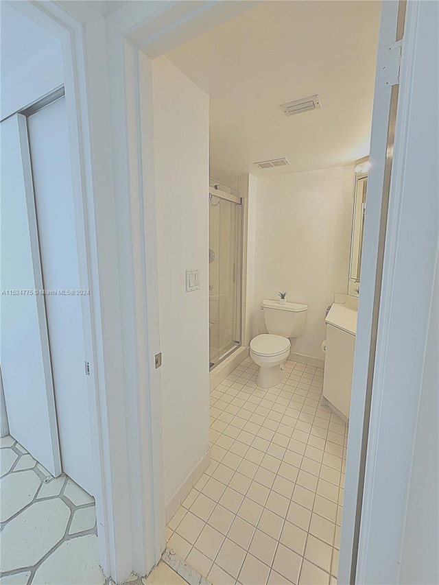 bathroom with tile flooring, toilet, and a shower with shower door