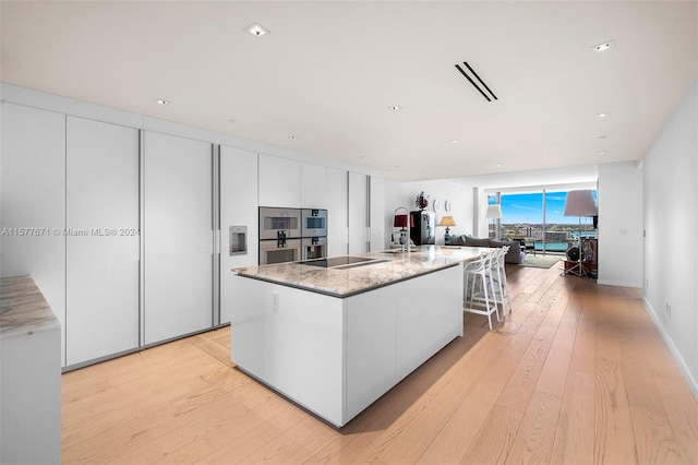 kitchen with white cabinets, light hardwood / wood-style floors, a center island with sink, and stainless steel double oven