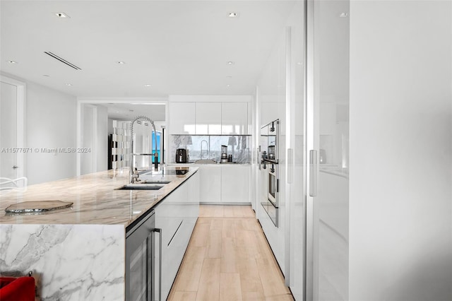 kitchen with beverage cooler, sink, white cabinetry, light hardwood / wood-style flooring, and light stone countertops