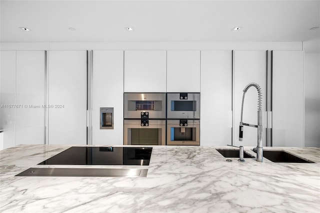 kitchen featuring double oven, white cabinets, sink, and light stone countertops