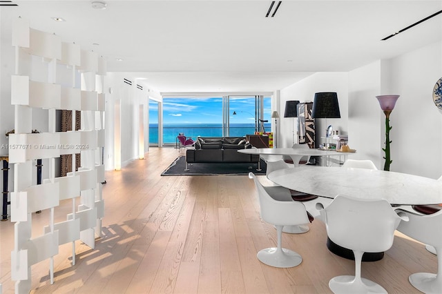 dining room with light hardwood / wood-style floors, a water view, and expansive windows