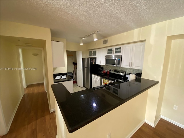 kitchen with a textured ceiling, dark hardwood / wood-style floors, white cabinets, kitchen peninsula, and stainless steel appliances