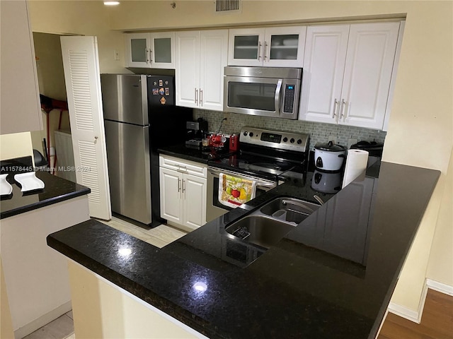 kitchen with sink, kitchen peninsula, backsplash, white cabinetry, and appliances with stainless steel finishes