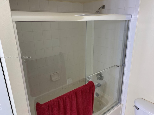 bathroom featuring toilet and combined bath / shower with glass door