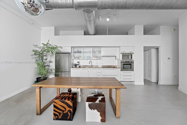 kitchen with sink, a towering ceiling, appliances with stainless steel finishes, concrete floors, and white cabinetry