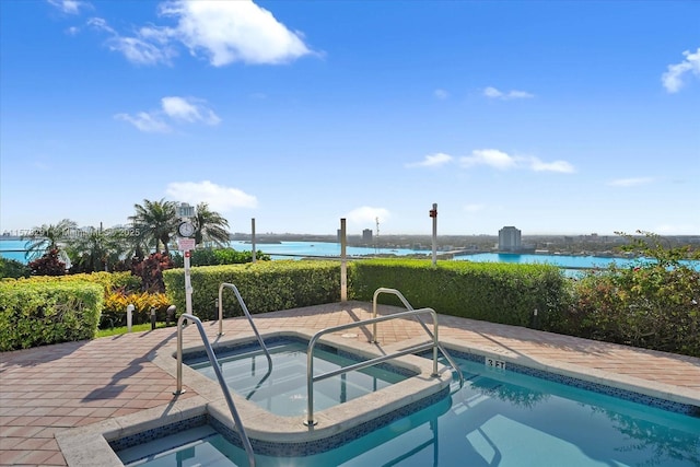 view of pool featuring an in ground hot tub, a water view, and a patio area