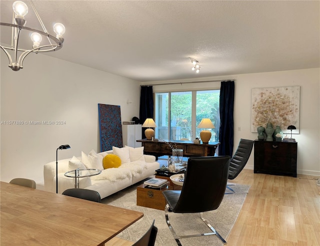 living room with a textured ceiling, a notable chandelier, light hardwood / wood-style floors, and track lighting