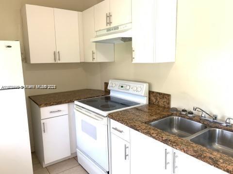 kitchen featuring white cabinets, white appliances, light tile flooring, sink, and dark stone countertops