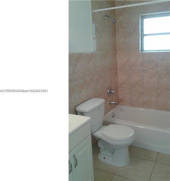 full bathroom with tiled shower / bath combo, tile walls, vanity, tile flooring, and toilet