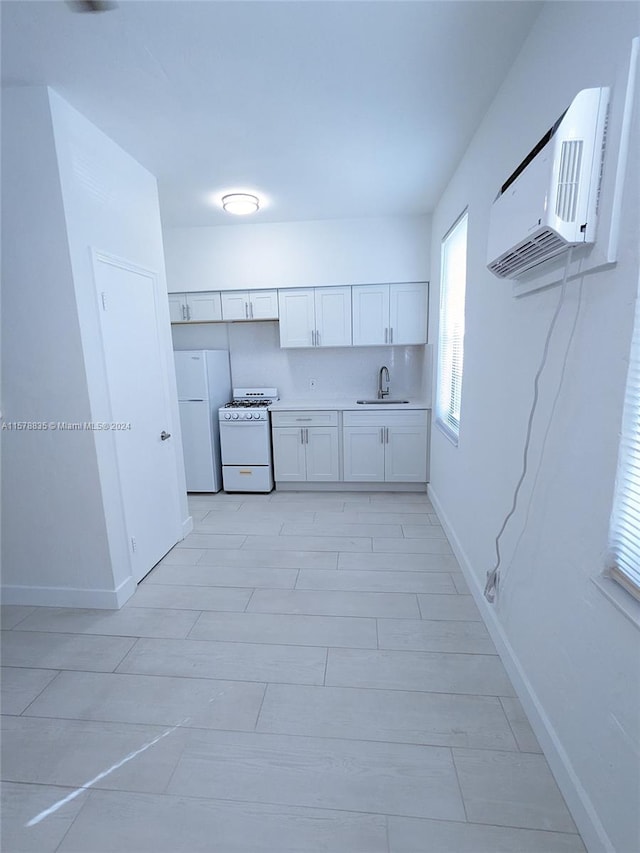 kitchen with an AC wall unit, white cabinets, sink, white appliances, and light tile floors