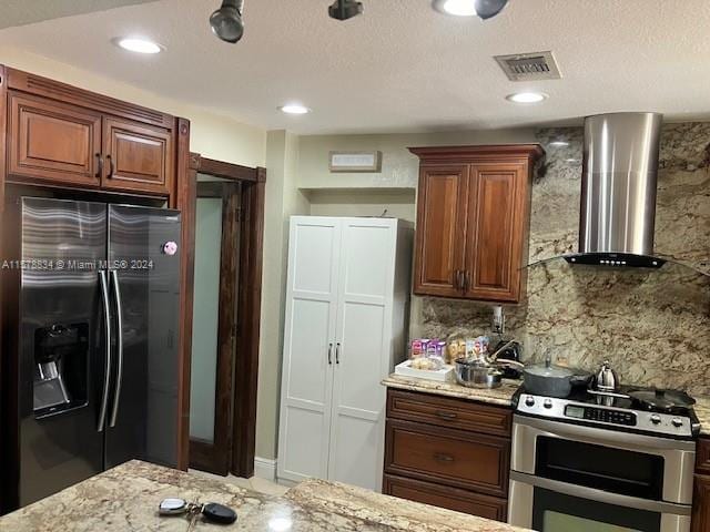 kitchen featuring a textured ceiling, light stone countertops, backsplash, appliances with stainless steel finishes, and wall chimney range hood