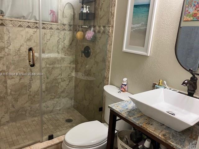 bathroom with a shower with shower door, toilet, and sink