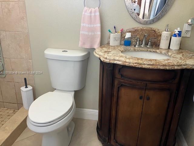 bathroom featuring vanity, toilet, tiled shower, and tile patterned flooring