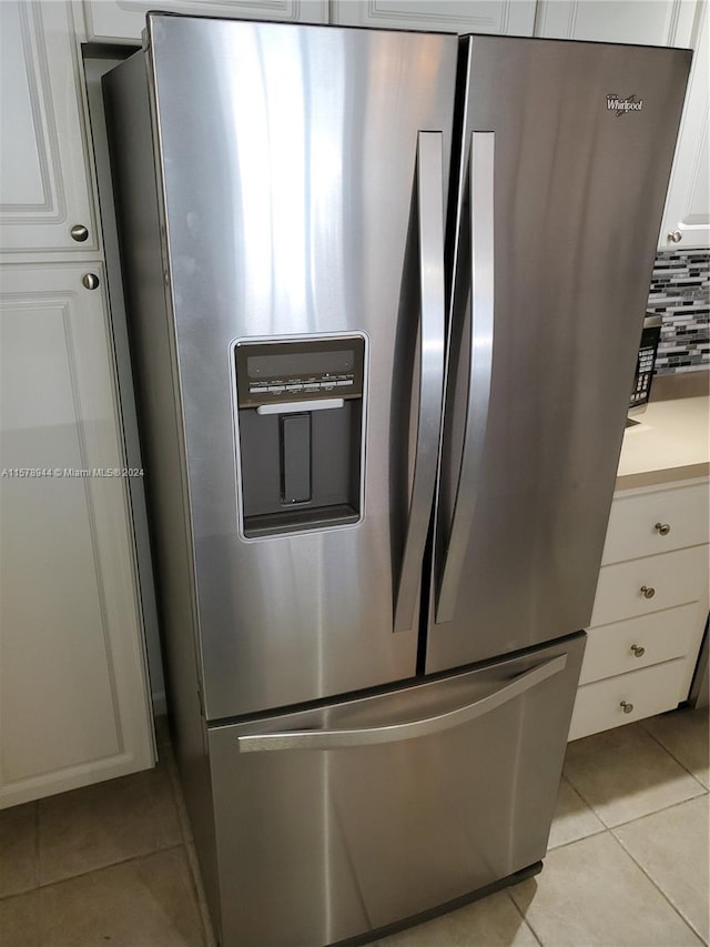 kitchen featuring stainless steel fridge, white cabinetry, light tile patterned floors, and tasteful backsplash