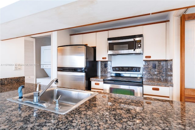 kitchen featuring white cabinetry, backsplash, stainless steel appliances, sink, and stacked washer and dryer