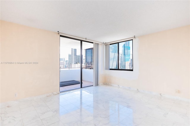 empty room featuring floor to ceiling windows, a textured ceiling, and light tile flooring