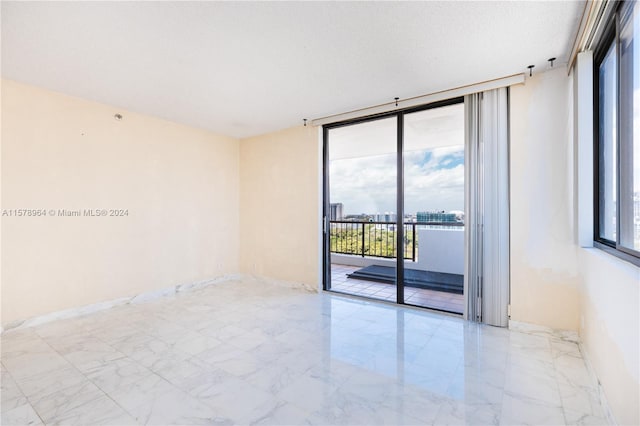 spare room featuring a wall of windows, light tile floors, and a textured ceiling