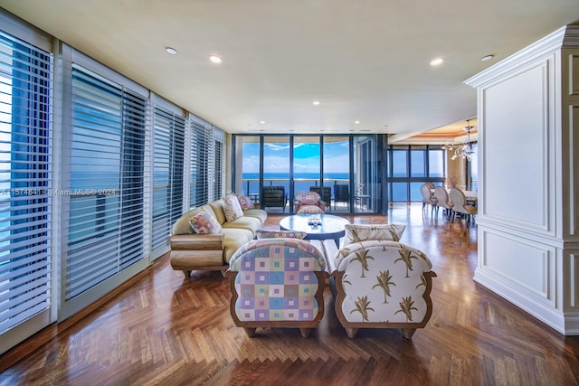 living room featuring dark parquet flooring, a water view, an inviting chandelier, and a wall of windows