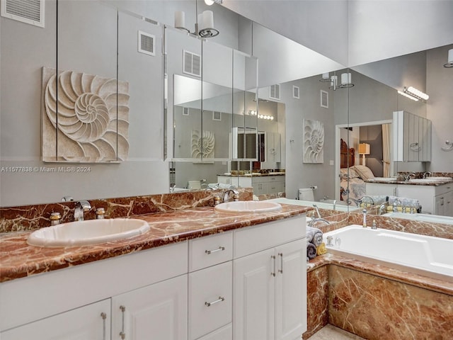 bathroom with dual sinks, tiled tub, large vanity, and an inviting chandelier