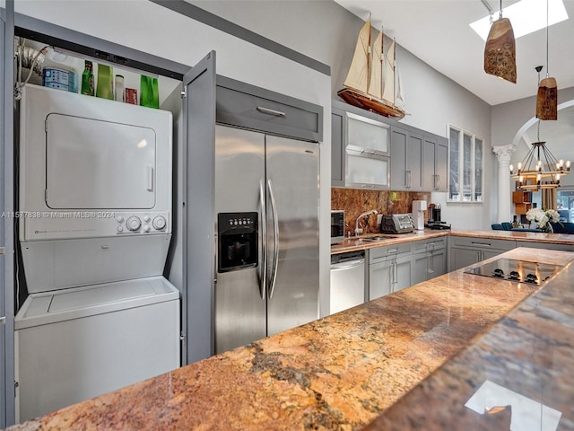 kitchen featuring pendant lighting, gray cabinets, stacked washer / dryer, backsplash, and appliances with stainless steel finishes