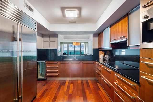 kitchen featuring built in fridge, dark hardwood / wood-style flooring, tasteful backsplash, and beverage cooler