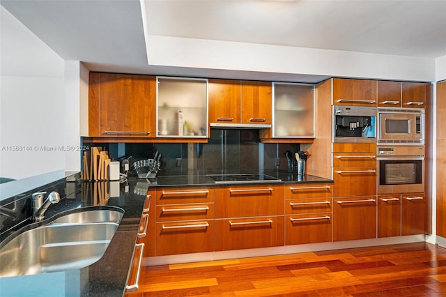 kitchen with dark stone counters, dark hardwood / wood-style flooring, backsplash, sink, and appliances with stainless steel finishes