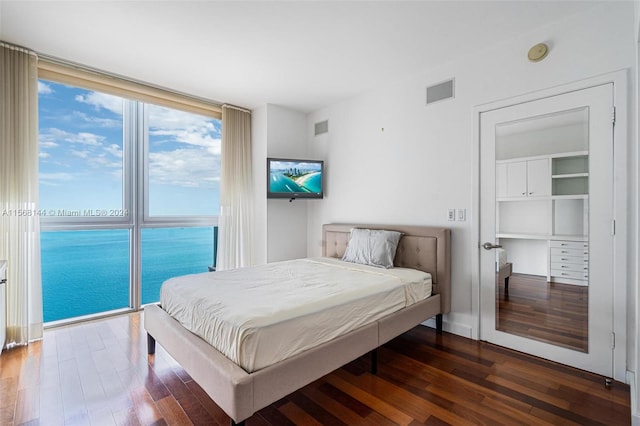 bedroom with a water view, dark hardwood / wood-style flooring, and a wall of windows