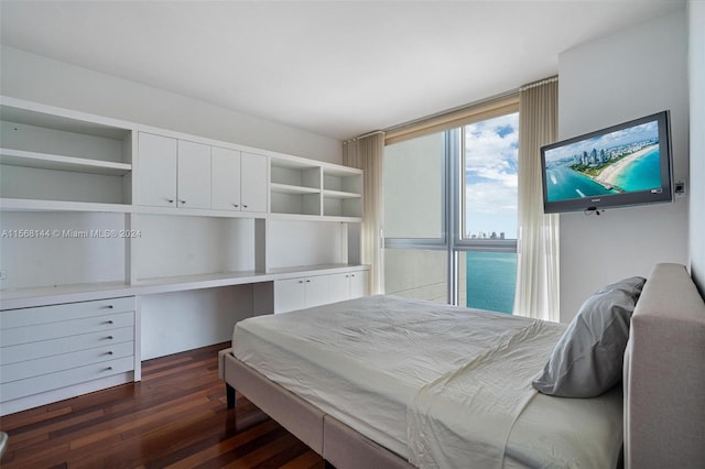 bedroom with dark wood-type flooring, a water view, and built in desk