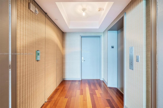 hall with a tray ceiling, hardwood / wood-style flooring, and elevator