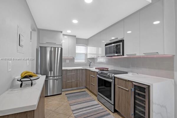 kitchen with appliances with stainless steel finishes, white cabinetry, wine cooler, light tile patterned flooring, and decorative backsplash