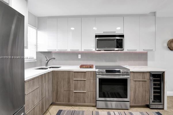 kitchen featuring white cabinetry, tasteful backsplash, beverage cooler, sink, and appliances with stainless steel finishes