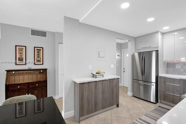 kitchen featuring decorative backsplash, white cabinetry, light tile patterned flooring, and stainless steel refrigerator