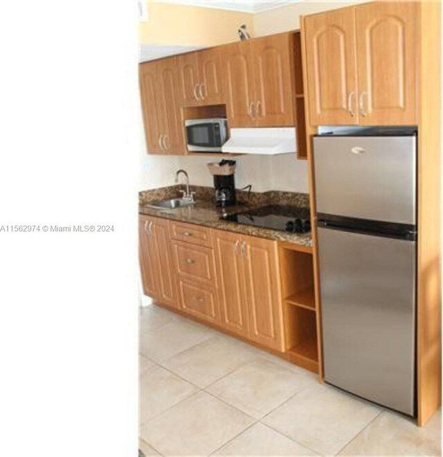 kitchen with sink, stainless steel fridge, black electric stovetop, light tile patterned flooring, and exhaust hood