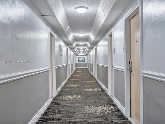 hallway with dark colored carpet and a textured ceiling