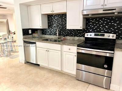 kitchen with appliances with stainless steel finishes, sink, light tile flooring, white cabinetry, and ventilation hood