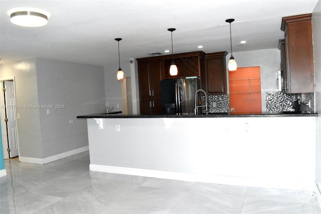 kitchen featuring kitchen peninsula, tasteful backsplash, fridge, decorative light fixtures, and light tile floors