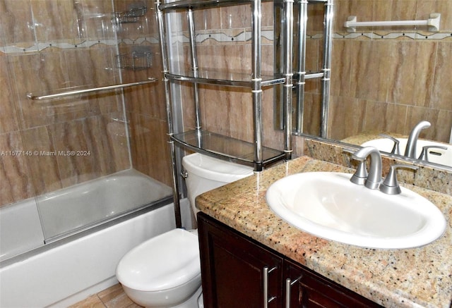 full bathroom with tile walls, combined bath / shower with glass door, toilet, and vanity