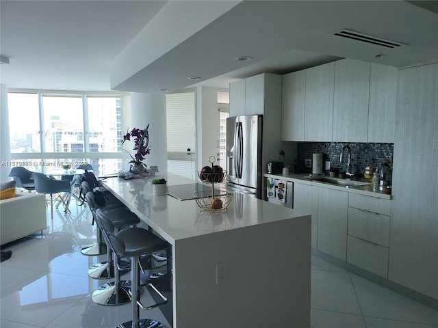 kitchen featuring sink, a kitchen bar, a wall of windows, decorative backsplash, and stainless steel refrigerator with ice dispenser