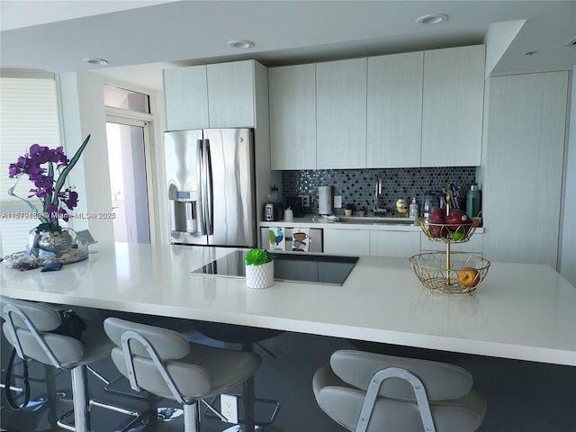 kitchen with stainless steel fridge with ice dispenser, tasteful backsplash, black electric stovetop, a breakfast bar area, and sink